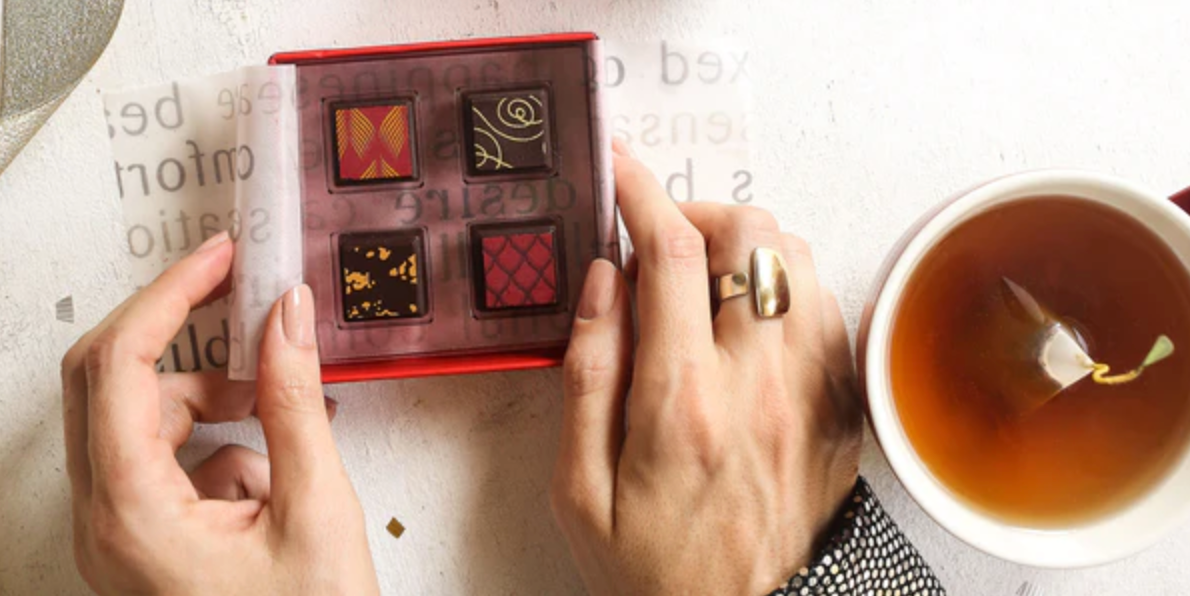 A cup of tea next to a box of chocolate pieces sitting on a table. Celebrating Easter, Easter gifts and chocolate